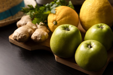 Composition of fruits, still life. Components of Asian cuisine. Lemon with ginger and green apples and herbs on a wooden board and on a dark background