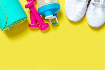 Flat Lay Sport and fitness equipment, pink dumbbells, sneakers, water blender bottle and mint yoga mat on yellow background. Top view with copy space. Healthy lifestyle.