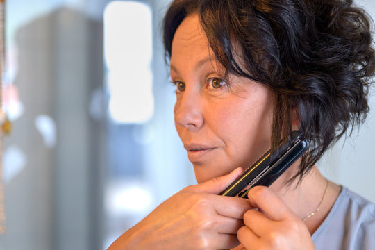 Middle-aged Hispanic Woman Using Curling Tongs