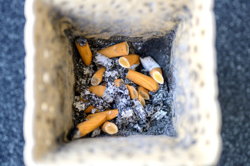 Old discarded cigarette stubs and ash in a bin