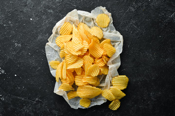 Delicious salty potato chips. Beer snacks on a black stone background. Top view. Free space for your text.