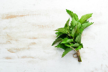 Fresh green nettles on a white wooden background. Healthy herbs. Top view.