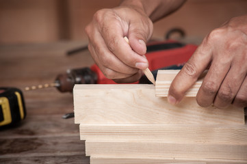 Hands of a carpenter taking measurement of a wooden plank