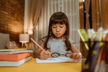 girl studying in the evening. asian little kid learning at home writing on a book