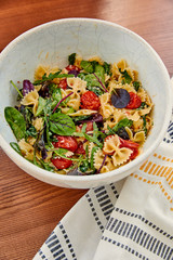 High angle view of bowl with tasty pasta salad near napkin on wooden background