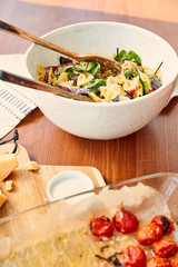 High angle view of bowl with pasta salad and ingredients on cutting board near napkin on wooden background