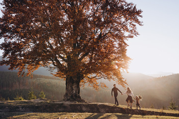Stylish young family in the autumn mountains. A guy and a girl with their daughter walk together...
