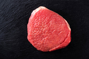 Raw meat steak on a black stone. Top view