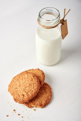 Cookies next to milk bottle with tag on white wooden table, 45 degrees view