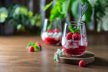 Homemade cottage cheese with fresh raspberries in a glass glass on a rustic wooden background. Dietary breakfast. Russian cottage cheese with berry and mint.