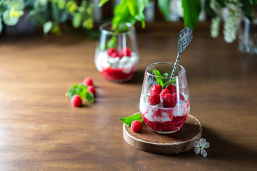 Homemade cottage cheese with fresh raspberries in a glass glass on a rustic wooden background. Dietary breakfast. Russian cottage cheese with berry and mint.