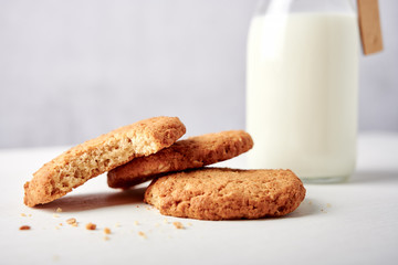 Cookies in front of milk bottle with tag on white wooden table against light grey grunge background, close-up side view
