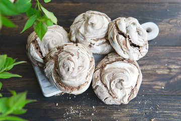 Homemade chocolate meringue cookies on rustic board, wooden table. Top view with green leaves. Italian or French dessert made of eggs and sugar. Natural light, copy space. 