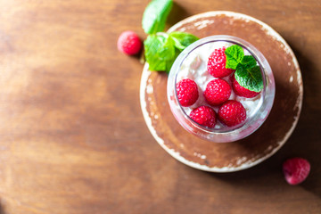Homemade cottage cheese with fresh raspberries in a glass glass on a rustic wooden background. Dietary breakfast. Russian cottage cheese with berry and mint.