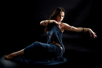 A tribal dancer in a dynamic sitting dance figure with a retro blue dress and many accessories.