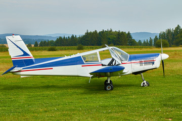 Fototapeta na wymiar Side view of Zlin Z-43 four-seat light airplane standing on a grass runway. Low-wing monoplane.