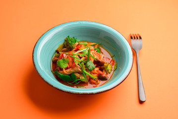 Meat salad with vegetable and fresh greenery served in a bowl isolated on bright orange background.