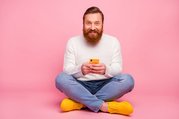 Full length photo of positive cheerful man sit floor legs crossed use cell phone read social media...