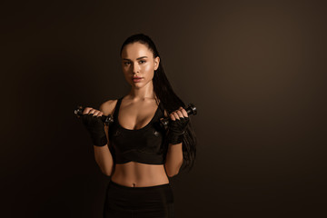Sportswoman training with dumbbells and looking at camera isolated on black