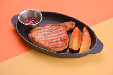 Rib eye steak served with baked potatoes and cranberry sauce on a black tray over light colorful background.