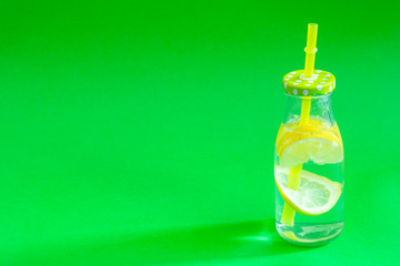 Lemonade in a glass bottle with a tube on an isolated green background, refreshing summer drink made of water ice and lemon