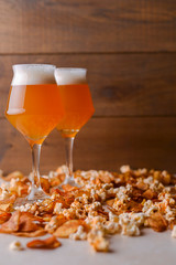 Two glass of beer and beer snacks over white and wooden background. Potato chips and salty popcorn.
