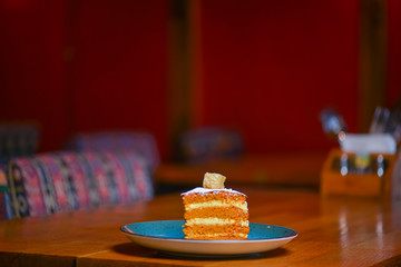 Slice of layered vanilla honey cake served on a blue plate on rustic wooden table over blurred restaurant background.