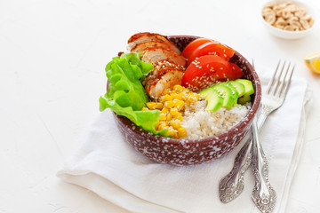 Buddha bowl with rice, tomatoes, corn, chicken and avocado on a napkin on a white table
