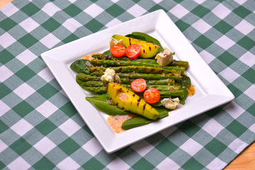 Healthy grilled avocado and asparagus salad with linen seeds and tomatoes. Served on a white square plate.