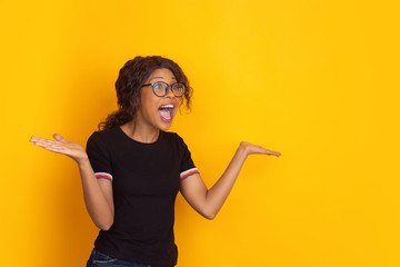 Fototapeta na wymiar Crazy shocked, astonished. African-american young woman's portrait isolated on yellow studio background. Beautiful female curly model. Concept of human emotions, facial expression, sales, ad, youth.