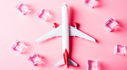 Travel concept. Model of airplane on pink background with ice cubes.