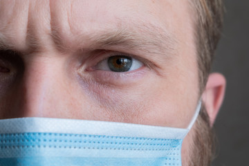 Close-up of a man's face in a protective blue mask. The guy's eye is an unusual color. Strict and serious male gaze.