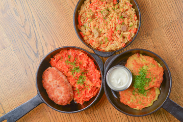 Delicious potato pancakes with sour cream, rice with meat and vegetables and Chicken Kiev cutlet served in frying pans.