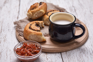 Variety of homemade puff pastry buns cinnamon served with milk cup, jam, butter as breakfast over white plank wooden background. Flat lay, space