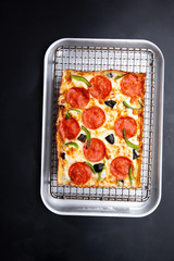 detroit pizza on an iron tray on a dark background. selective focus