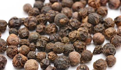 Whole black peppercorns on white background.