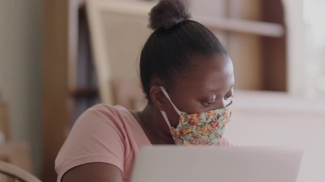 Close up of a young black female student working on her laptop while wearing a health mask.