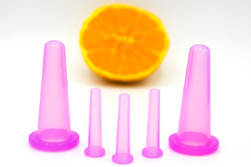 five different sized anti cellulite pink cosmetic vacuum jars for body and face with orange on white background. Close up. Home spa treatments.