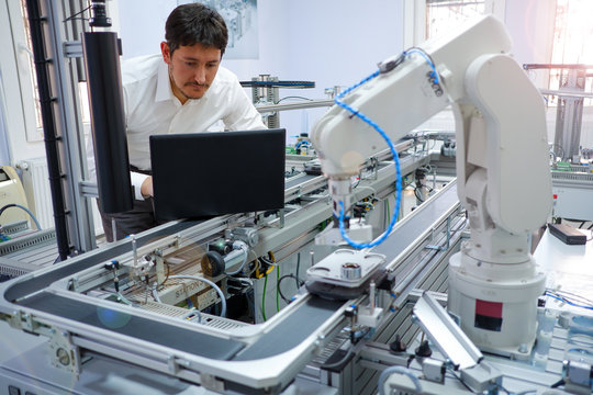 Close-up robot arm. Engineer is working on laptop to programming smart factory automation and automated car on production line. Industry 4.0 concept; artificial intelligence in smart factory.