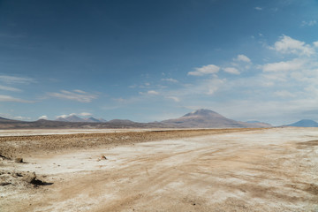 Dry, barren landscape mountain background.  Dramatic desert, snowcapped mountains wilderness. Mountain range view. Salt Flats of Uyuni, Bolivia. Copy space, blue sky, nature, hiking, and sand dust