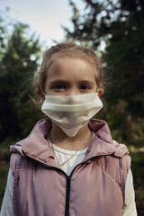 Portrait of a little girl in a protective medical mask in a park