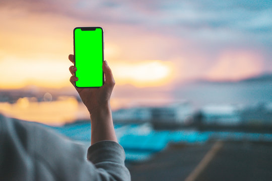 Hand holding a smartphone on a green screen