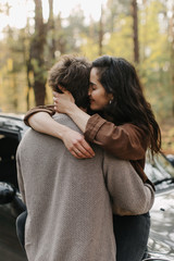 beautiful young couple in love kisses and hugs sitting on a car