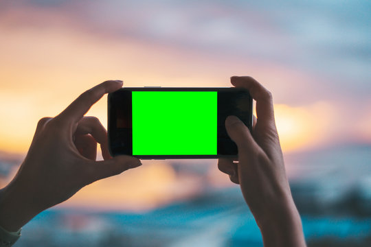 Pair of hands holding a smartphone on a green screen with 4:3 format