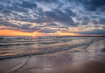 Baltic Sea panorama at sunset with shore waves and sun on the horizon.