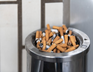 A full ashtray in front of a bright brick wall.