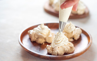 the process of creating Pavlova dessert, decorating the meringue with cream from the culinary bag