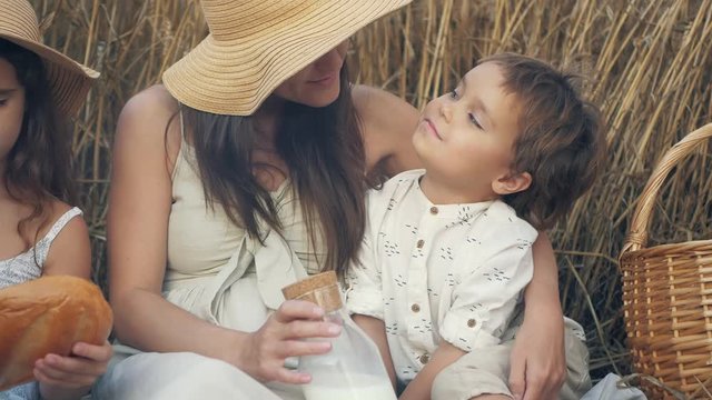 beautiful mother with children has lunch on the nature with bread and milk. Happy farm family picnicking in a wheat field. The concept of organic farming and a healthy lifestyle, a healthy and happy