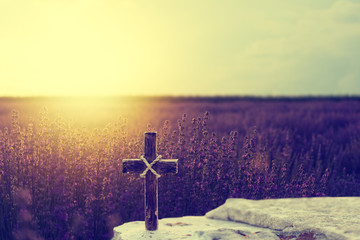 Wooden Christian cross on rocks against beautiful golden sunrise over lavender field