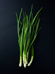 Bunch of scallions on black background, from above